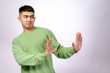 An Asian man in a green sweatshirt makes a disgusted expression while holding both hands up in a...