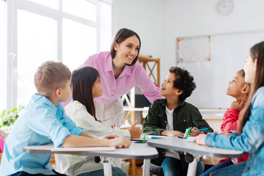 Group of diverse kids listening their friendly female teacher while sitting at desks in classroom, creating positive atmosphere