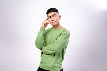 An Asian man in a green sweatshirt poses thoughtfully with a finger on his temple and a serious...