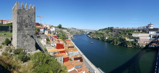 Panorama de cidade europeia, com torre medieval, e rio de águas azuis refletindo a cor do céu.