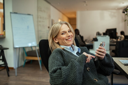 Smiling young woman using smartphone in modern office