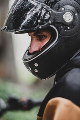 Fototapeta premium Hombre adulto en motocicleta negra por camino rodeado de arboles en día lluvioso