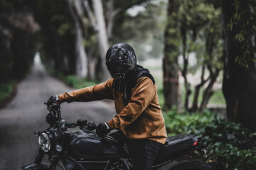 Hombre adulto en motocicleta negra por camino rodeado de arboles en día lluvioso