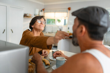 Elderly woman playfully feeding her partner a pastry at home