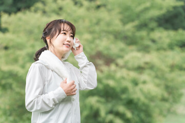 公園でウォーキング・運動をする汗をタオルで拭くスポーツウェアのアジア人女性
