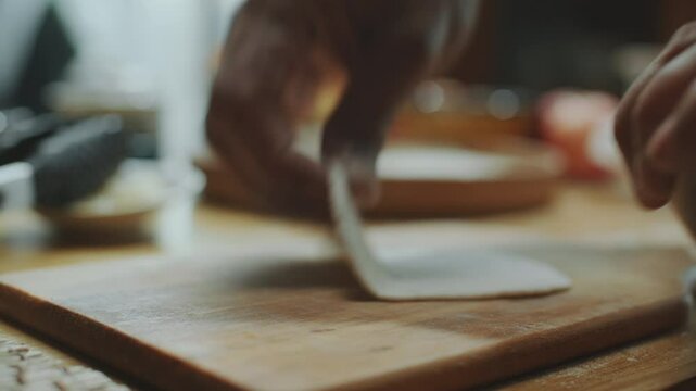 Hands of unrecognisable man using rolling pin to flatten dough into round thin sheet on table to make traditional Indian bread. Close-up shot