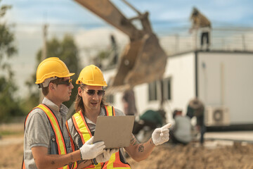 Workers in safety vests and helmets reviewing construction plans at a job site, highlighting...