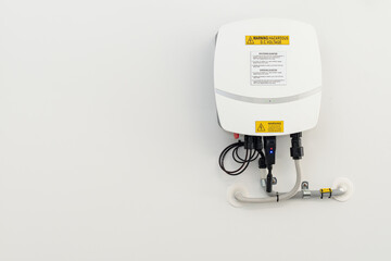 Solar inverter equipment attached to a white wall with cables connections warning lables and green lights showing energy produced offset to right  side giving space for copy