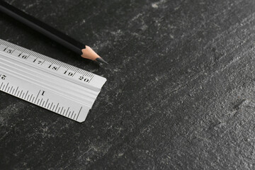 Metal ruler and pencil on black table, closeup. Space for text