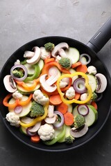 Frying pan with mix of vegetables and mushrooms on grey table, top view