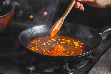 Chef adding spices paprika to frying pan while cooking delicious meal