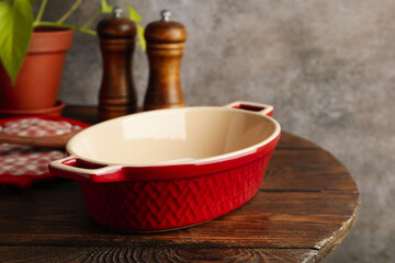 Ceramic casserole, potholder and shakers on wooden table, closeup