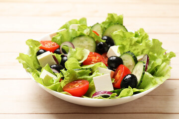 Delicious fresh Greek salad on light wooden table, closeup