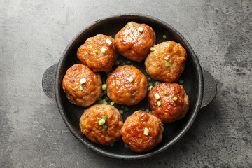 Tasty meatballs with green onion in baking dish on grey table, top view