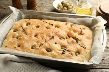 Delicious focaccia bread with olives and thyme on wooden table, closeup