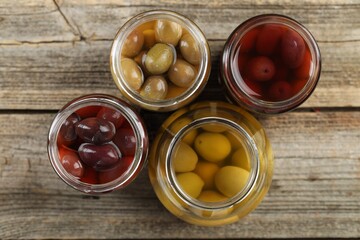 Pickled olives in glass jars on wooden table, flat lay