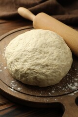 Fresh dough and rolling pin on wooden table, closeup