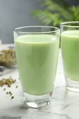 Fresh mung bean juice in glasses and seeds on white marble table, closeup