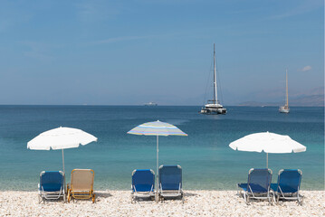 Beach umbrellas and beach chairs with boats on the sea in the background