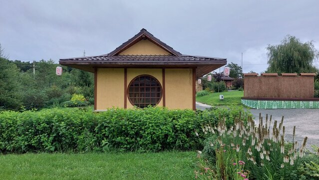 Traditional Japanese garden pavilion surrounded by lush greenery and trees with sunlight filtering through. Zen and tranquility concept for design and print