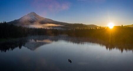 Sunrise over a tranquil Trillium Lake, Mt. Hood in the background. Fishermen in a small boat enjoy the peaceful morning.  Oregon, United States