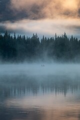 Fototapeta premium Misty morning on Trillium Lake. Two fishermen in a small boat, silhouetted against the fog. Peaceful scene. Oregon, United States
