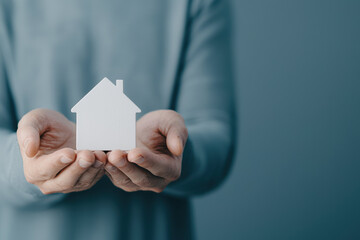 person holding small white house model, symbolizing warmth and security