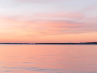 Obraz premium A serene pastel sunset over a calm lake, with soft hues of pink, lavender, and peach reflecting on the water s surface