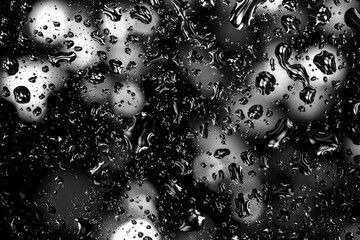 Close-up of black and white water droplets on glass, creating a dramatic and moody abstract...