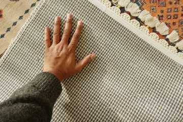Hand touching textured fabric on woven rug indoors