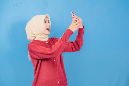 A woman in a red sweater is holding a cell phone and smiling. She is happy and excited about something on her phone