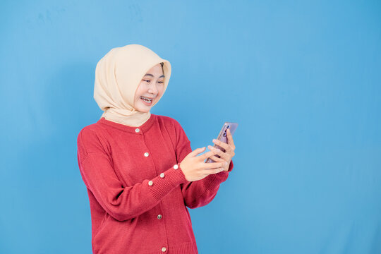 A woman in a red sweater is holding a cell phone and smiling. She is happy and excited about something on her phone