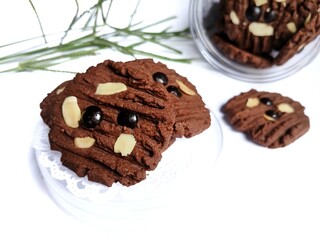 A jar of chocolate cookies and artificial flowers on a white background. Eid al-Fitr celebration.
