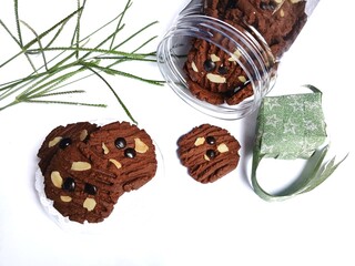 A jar of chocolate cookies, green ribbon diamonds, and artificial flowers  on a white background. Eid al-Fitr celebration.
