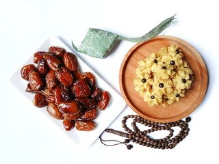 Delicious semprit rose cookies or rose butter cookies with chocochips on wooden plate, dates, prayer beads and green ribbon ketupat on white background.