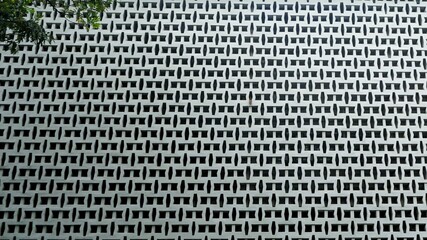 A modern architectural wall with a repeating geometric pattern, creating depth and symmetry. The hollow blocks allow light and air to pass through, blending functionality with aesthetic appeal.