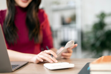Young woman counting bills for payment on a calculator at home.