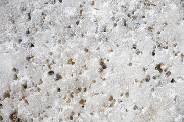 Melting ice with embedded gravel creates a unique, textured surface, as patches of stone emerge through the translucent ice, highlighting the transition from winter to spring.