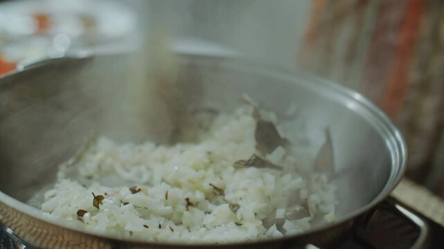 Close-up shot of using spatula to stir chopped onions with whole spices such as cumin and bay leaves in hot cooking pan as preparing traditional Indian food