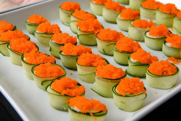 Cucumber rolls with flying fish roe on a white plate.
