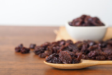 Raisins in wooden spoon on wooden table background. Raisins in bowl. Raisins spilling out of jar. Dry raisins. Selective focus.