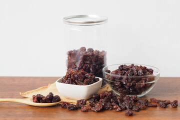 Raisins in bowl on wooden table background. Raisins in wooden spoon. Raisins spilling out of jar. Dry raisins.