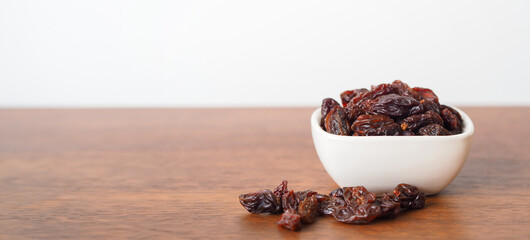 Raisins in white bowl on wooden table background. Dry raisins.