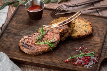 Grilled pork steak on a bone with potato patties served on a wooden cutting board with pepper and salt