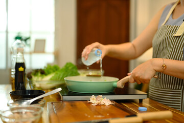 Close up of woman adding water into a pan while cooking on an induction stove