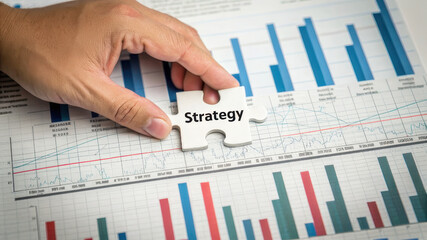 Hand placing puzzle piece labeled strategy on financial graphs and charts. , Recession concept