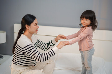 mother and toddler baby girl holding hands on bed