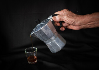 A man pouring coffee from moka pot into cup on table. 