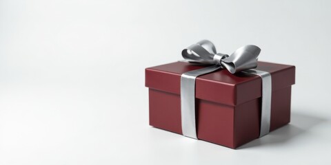 Fototapeta premium A maroon gift box with a silver ribbon and bow, sitting on a white surface, presents a celebratory mood