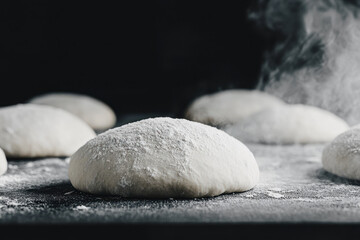 Raw dough balls rising with steam on a dark background, ready for baking